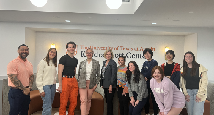 A group photo of UT Austin students posing with Patti DeNucci in front of the Kendra Scott Center sign