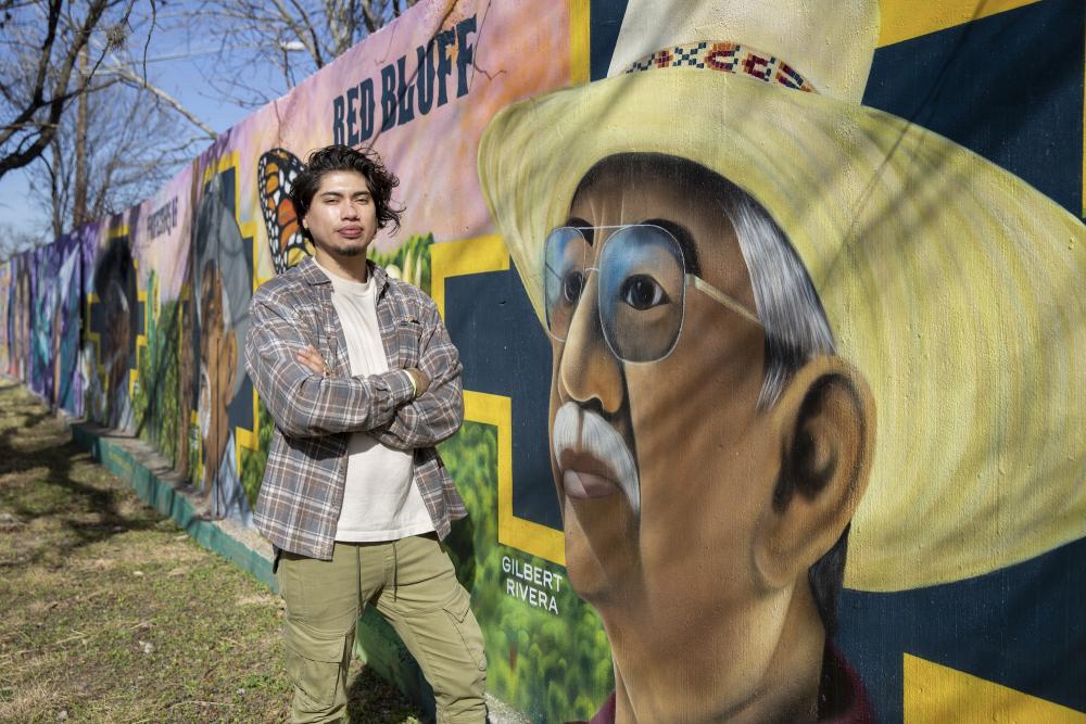 Artist Ruben Esquivel standing next to mural Protectors of the Red Bluff